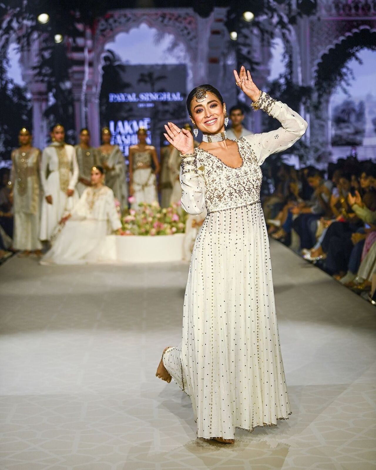 Shriya's outfit was a sight to behold. The ivory organza anarkali kurta and churidar set sparkled with gold sequins, while solitaire diamond studs lined the skirt, adding both volume and a magical effect. The churidar was also embellished with gold and diamonds around the ankles, complementing the rich design